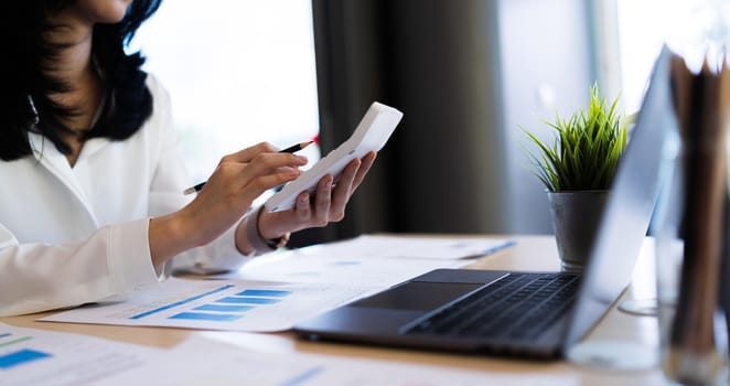 Business Woman or Young entrepreneur hand holding pen and working with a calculator at the workplace. Financial and tax systems concept.