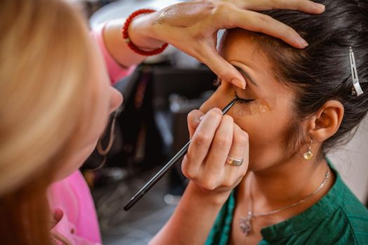 A portrait of a pretty woman having make-up applied by a makeup artist. Close-up.