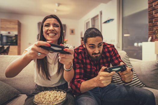 Excited couple is playing video games at home sitting on sofa. They have great weekend in nice company indoors. 