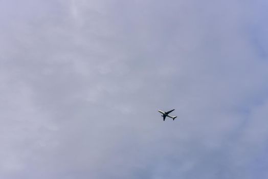 Passenger plane is flying far away against the blue summer and cloudy sky with copy space.