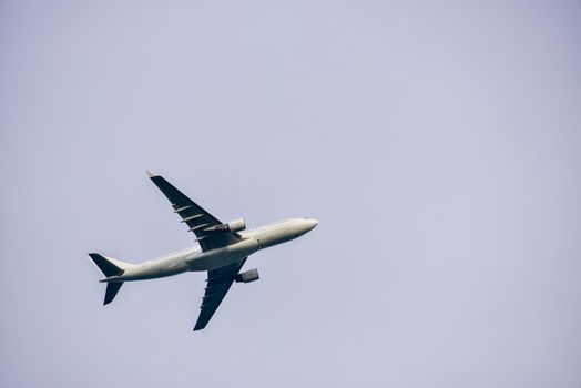 Passenger plane is flying far away against the blue summer and cloudy sky with copy space.