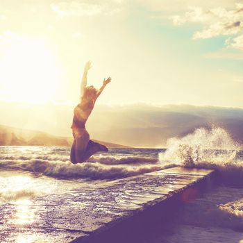 Feeling of freedom concept. Woman jump on pier facing to the sea with big waves.