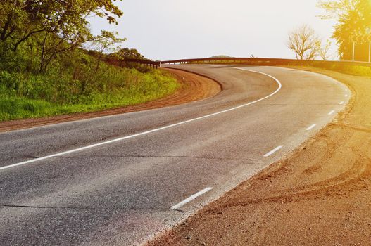 A winding road with tire tracks on the asphalt. A sharp turn with sunlight.