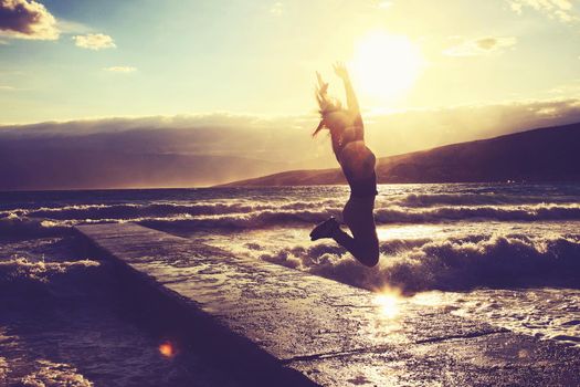 Feeling of freedom concept. Woman jump on pier facing to the sea with big waves.