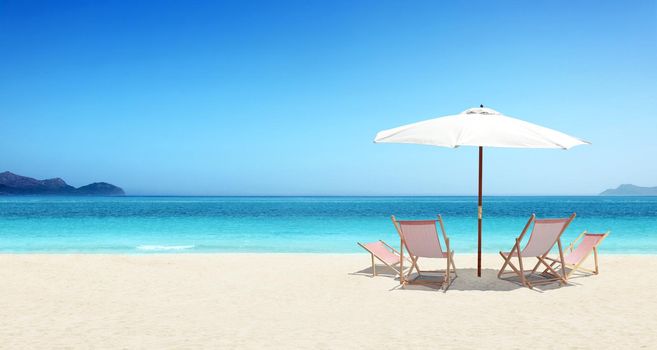 Wooden deck chairs on sandy beach near sea. Holiday background.