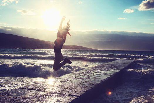 Feeling of freedom concept. Woman jump on pier facing to the sea with big waves.