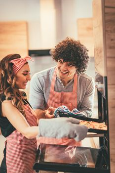 Young smiling happy couple put a pizza in the oven to bake, making fun.