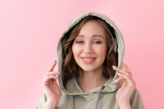 Happy teeth smile woman holds hood with his hands Caucasian female enjoy dressed oversize hoodie pink background close up portrait