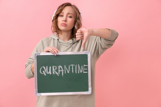 Stay home concept Woman with headphones dressed oversize hoodie holds chalkboard with the words quarantine. Coronavirus protection New normal concept Covid19 pandemic Social distancing work from home
