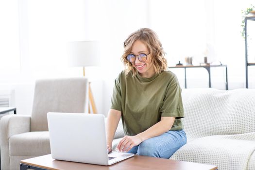 Woman with glasses use laptop typing keyboard sitting couch big window background home interior Freelance female working from home Distance learning student relaxing watch lessons video conference.