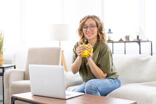 Woman with glasses use laptop typing keyboard sitting couch big window background home interior Freelance female working from home Distance learning student relaxing watch lessons video conference.