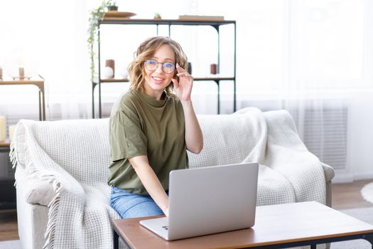 Woman with glasses use laptop typing keyboard sitting couch big window background home interior Freelance female working from home Distance learning student relaxing watch lessons video conference.