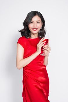 Young celebrating asian woman in red dress holding wine glass.