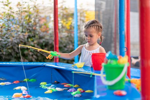 Child Fisher Catching Plastic Toy Fish On Pool Amusement Park Summer Day Little Girl Have Fun On Fishing Carnival Festival Entertainment For Children