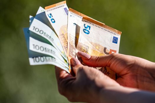 banknotes of 50 and 100 euros in the hands of a woman background in nature