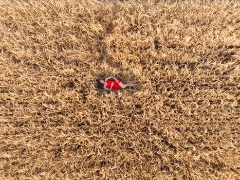 Aerial view of woman in red dress lying in the yellow field of wheat