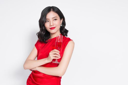 Young celebrating asian woman in red dress holding wine glass.