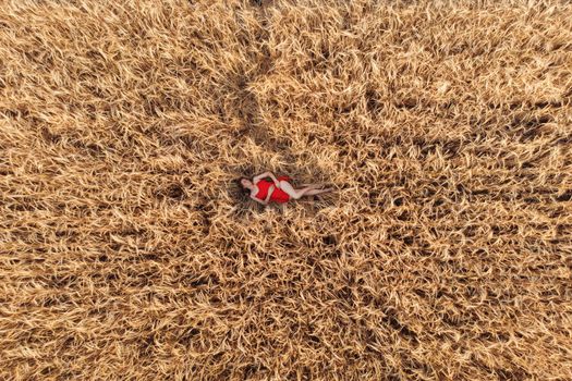 Aerial view of woman in red dress lying in the yellow field of wheat