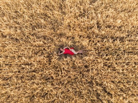 Aerial view of woman in red dress lying in the yellow field of wheat