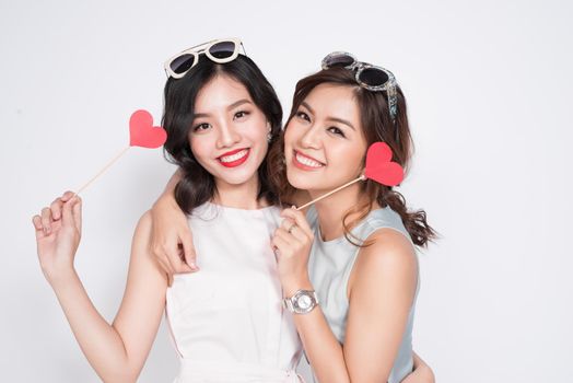 Two fashionable women in nice dresses standing together and holding red heart shape.