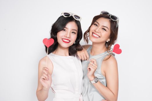 Two fashionable women in nice dresses standing together and holding red heart shape.