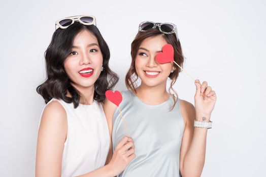 Two fashionable women in nice dresses standing together and holding red heart shape.