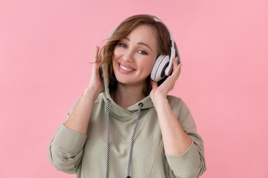 Happy teeth smile woman listen music headphones Caucasian female enjoy podcast or audio books dressed oversize hoodie pink background close up portrait