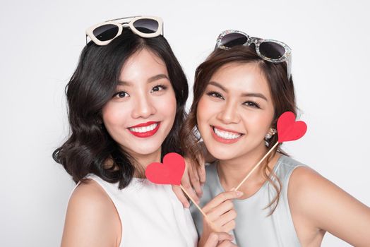 Two fashionable women in nice dresses standing together and holding red heart shape.