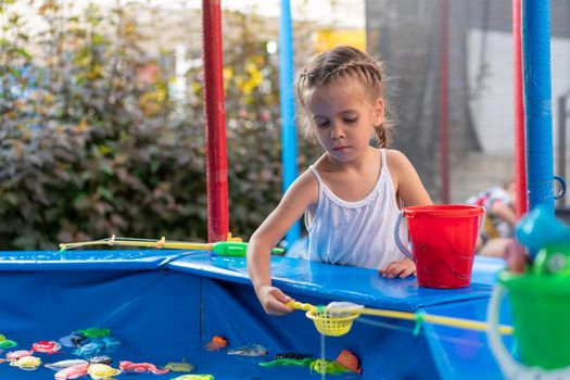 Child Fisher Catching Plastic Toy Fish On Pool Amusement Park Summer Day Little Girl Have Fun On Fishing Carnival Festival Entertainment For Children