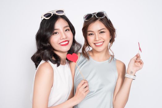 Two fashionable women in nice dresses standing together and holding red heart shape.