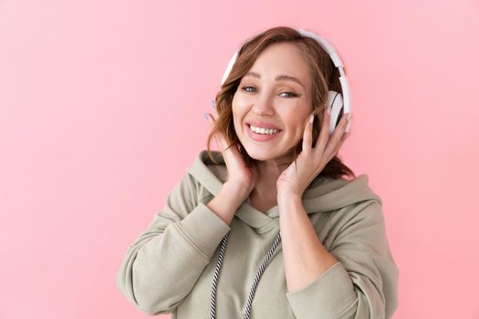 Happy teeth smile woman listen music headphones Caucasian female enjoy podcast or audio books dressed oversize hoodie pink background close up portrait
