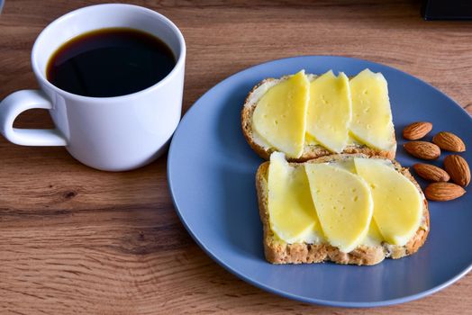 A cup of coffee, toast with cheese and almonds on a plate, stand on a wooden table.