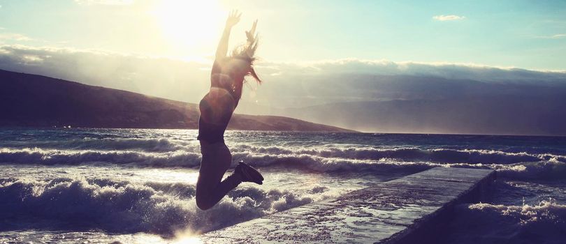 Feeling of freedom concept. Woman jump on pier facing to the sea with big waves.