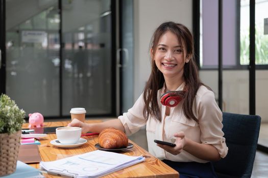 Beautiful young Asian girl working at a office space with a mobile phone. Concept of smart female business accounting.