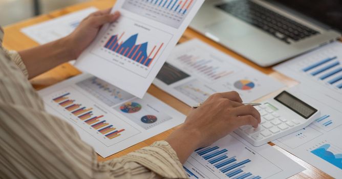 Close up of businessman or accountant hand holding pen working on calculator to calculate business data, accountancy document and laptop computer at office, business concept