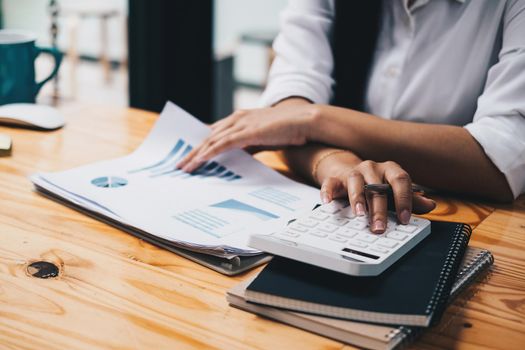 Close up asian female accountant or banker making calculations with calculator. Savings, finances and economy concept through a laptop.