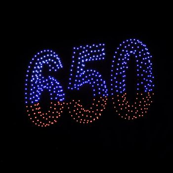 Colorful drone light shows on black night sky background. A figure of the number six, five, zerro, 650 made of glowing drones.