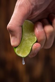 Hand squeeze lime with lime drop on dark wooden background