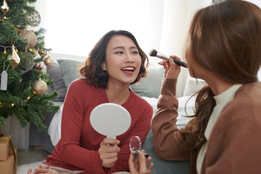 young girl friends sitting on living room floor and applying make up cosmetics in cozy apartment.
