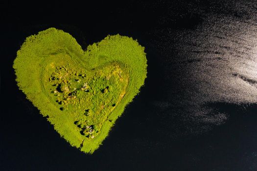 Love island on a lake in Europe, a Green heart-shaped Island on a dark lake with a sparkle from the sun.