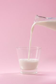 Pouring milk in to glass from bottle on a pink