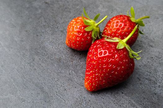 Three  red ripe strawberries over dark background with copy space