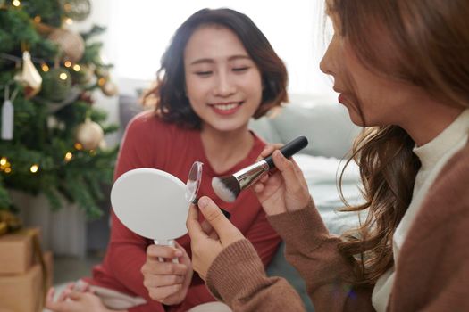 Creative young woman applying make-up on friend's face in sitting room