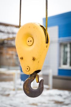 Yellow constraction crane hook with some industrial buildings on the background