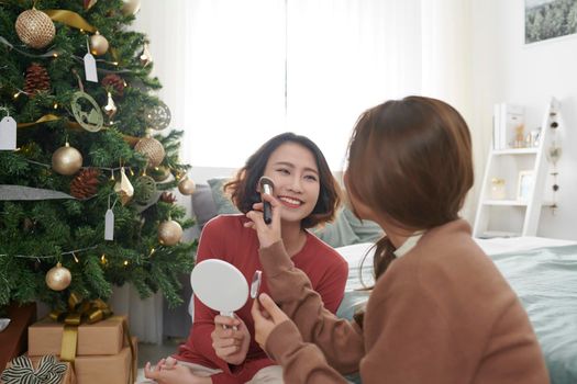 Two modern girls applying make up and helping each other at bed room