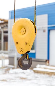 Yellow constraction crane hook with some industrial buildings on the background