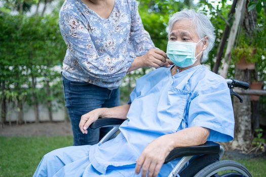 Help Asian senior or elderly old lady woman on wheelchair and wearing a face mask for protect safety infection Covid-19 Coronavirus in park.