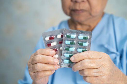 Asian senior or elderly old lady woman patient holding antibiotics capsule pills in blister packaging for treatment infection patient in hospital, Pharmacy drugstore concept. Pharmacy drugstore concept.