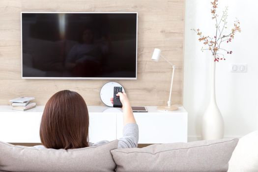 Young woman watching TV in the living room. Back view