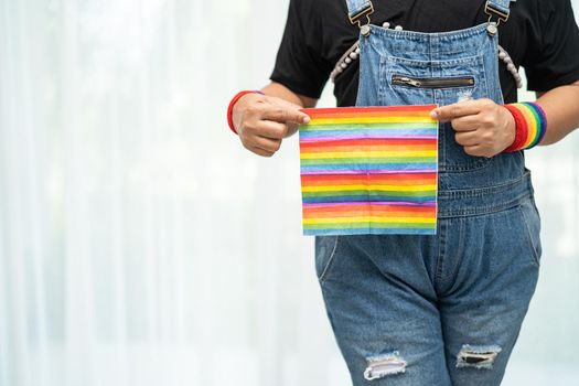 Asian lady wearing blue jean jacket or denim shirt and holding rainbow color flag, symbol of LGBT pride month celebrate annual in June social of gay, lesbian, bisexual, transgender, human rights.